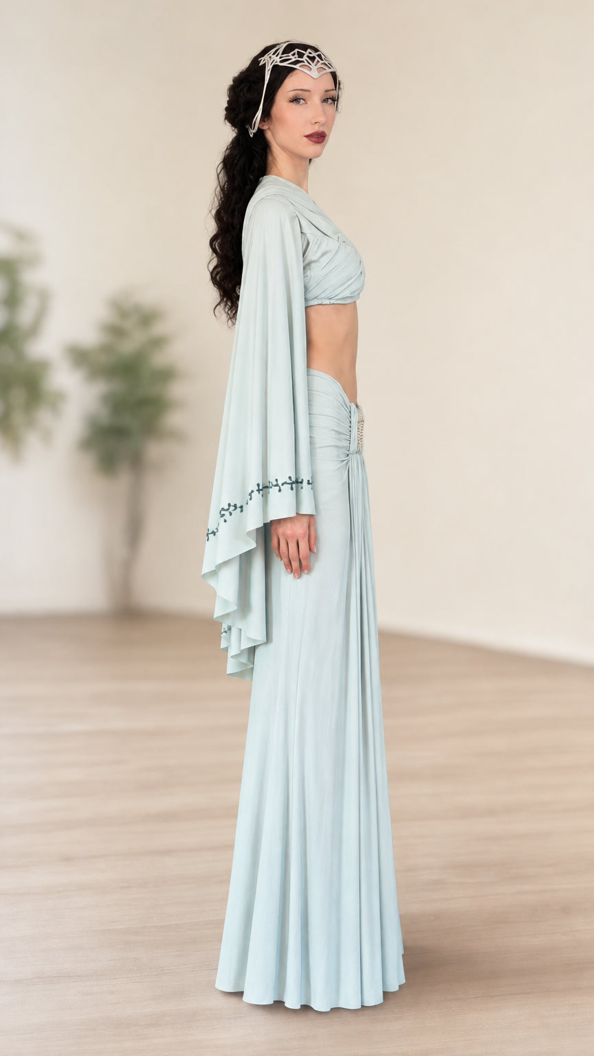 Side profile of model wearing light blue two-piece crop top and maxi skirt set with draped cape sleeves