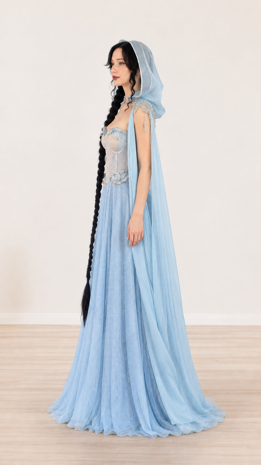 Side profile view of light blue hooded evening gown highlighting structured bodice and cape