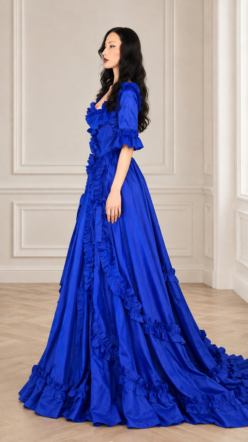 Side angle view of royal blue floor-length Victorian dress showing ruffle tiers