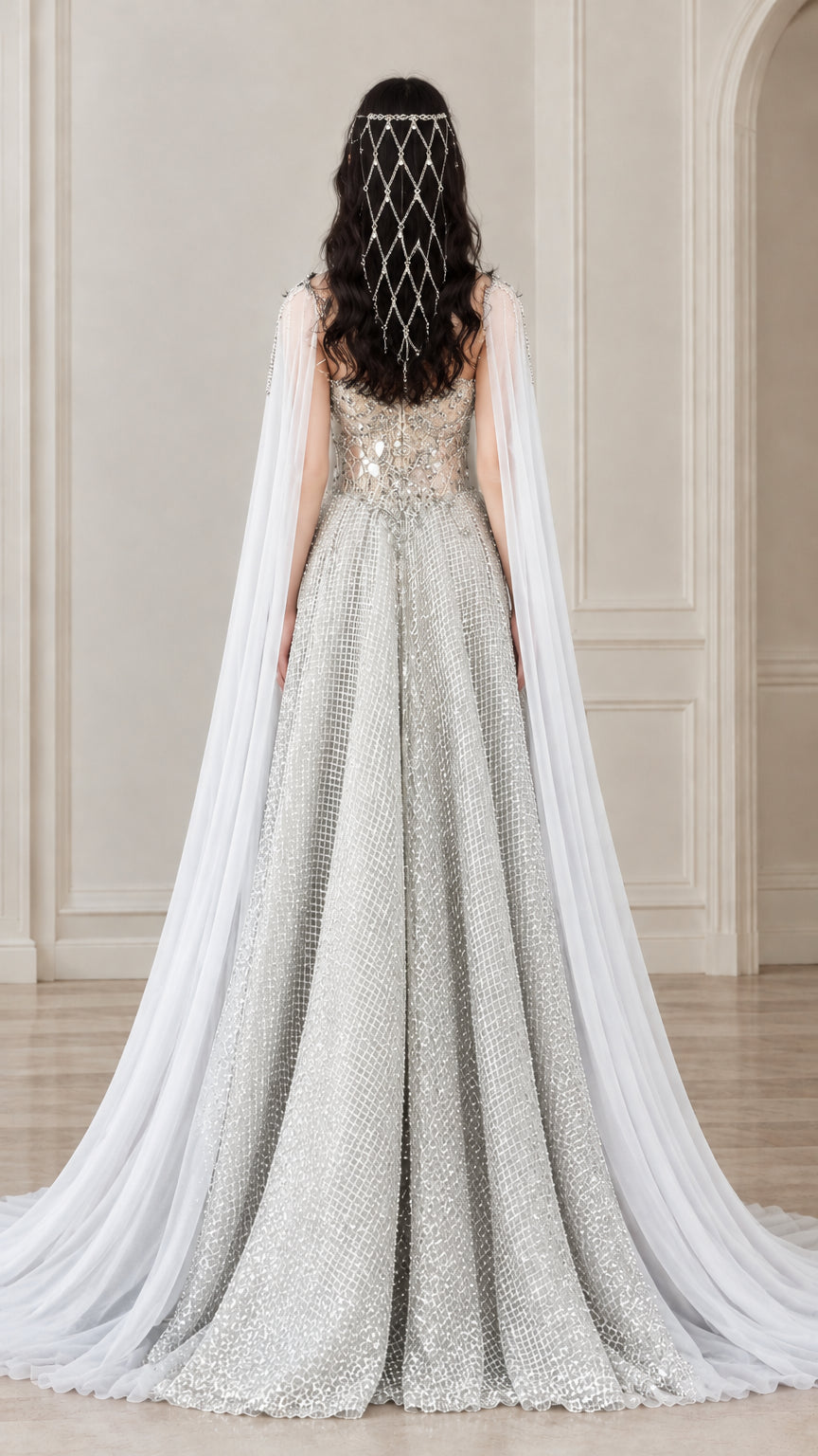 Back view of silver formal evening gown highlighting the extended sheer cape and glitter grid skirt