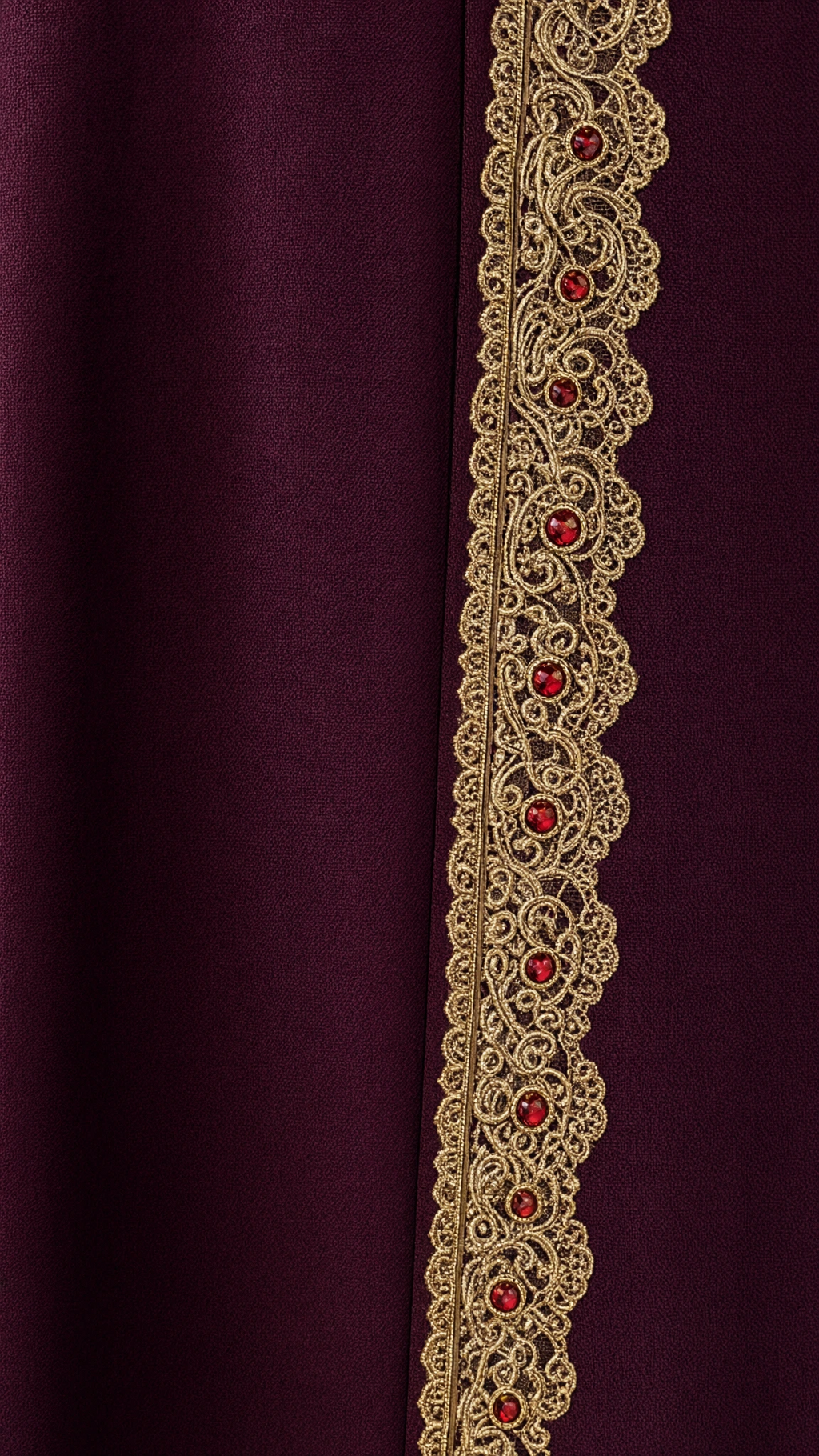 Close-up detail of gold embroidered lace trim with ruby jewel accents on burgundy fabric