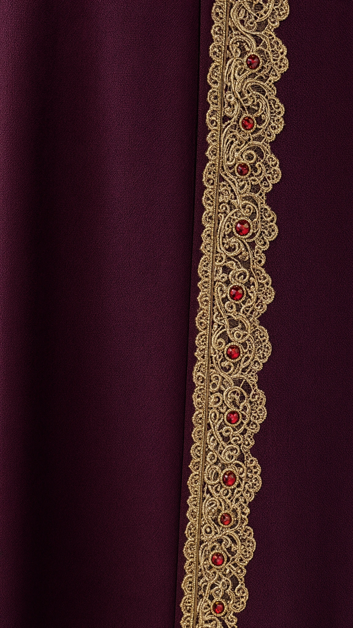 Close-up detail of gold embroidered lace trim with ruby jewel accents on burgundy fabric